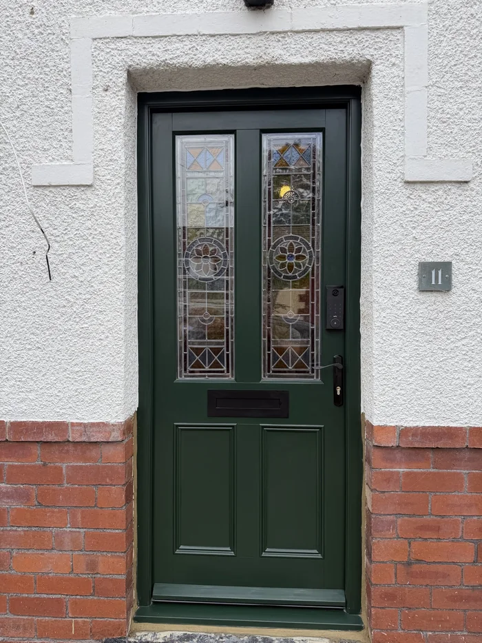 Dark green entrance door with two decorative glazed panels and a black lever handle