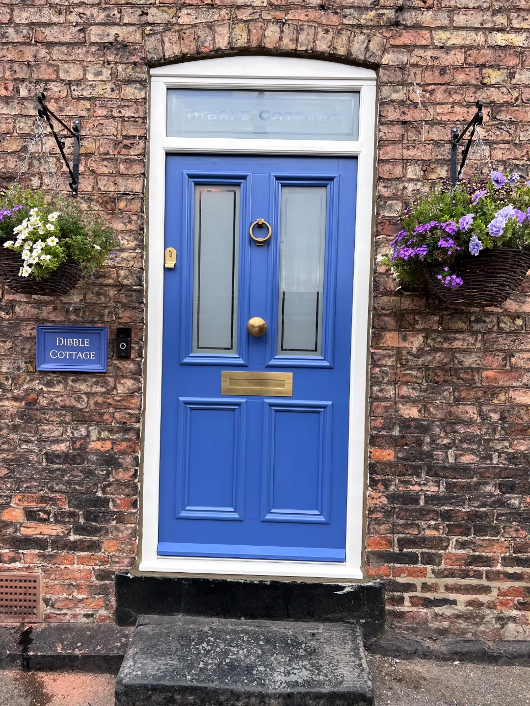Cornflower blue cottage front door with brass ring knocker and hanging baskets — Dibble Cottage, Leeds. Bespoke heritage door by Bailey Hague Joinery.