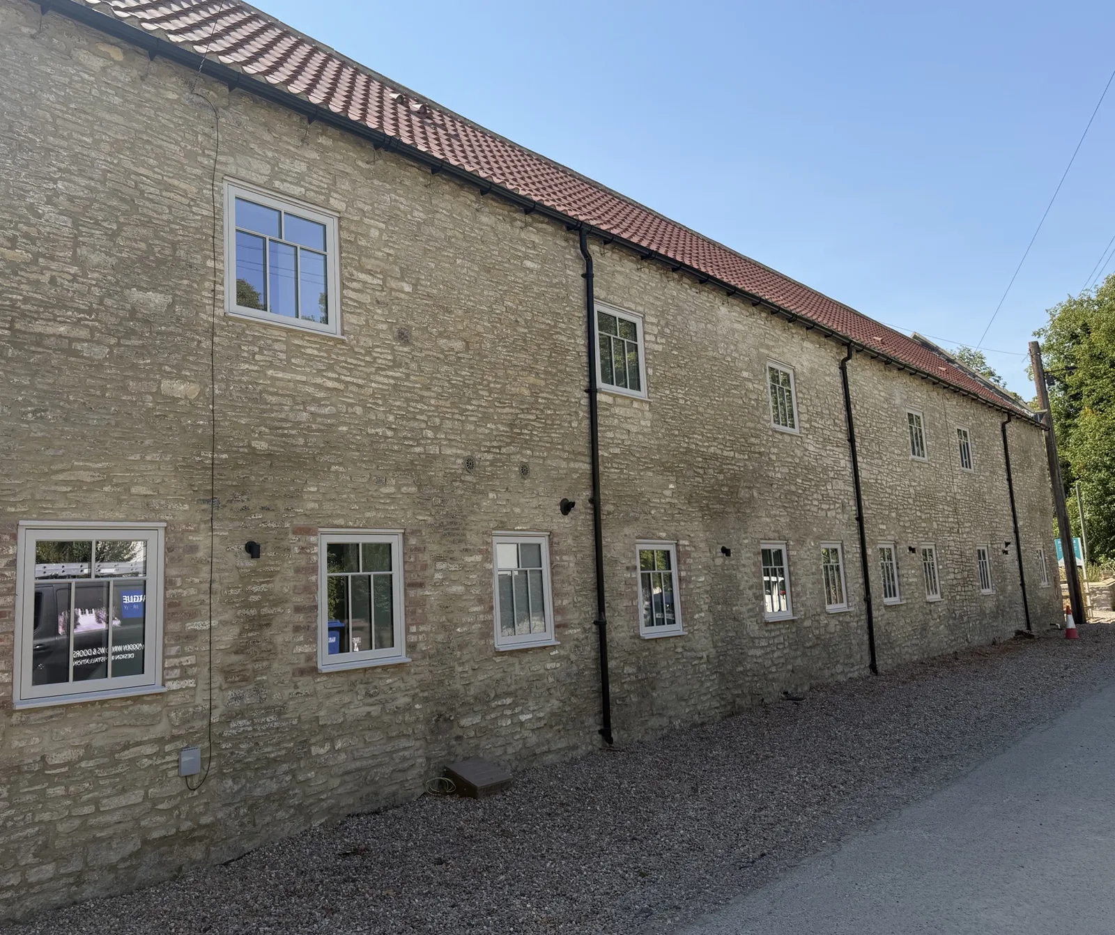 Long stone barn elevation with small hardwood casement windows set into the original openings