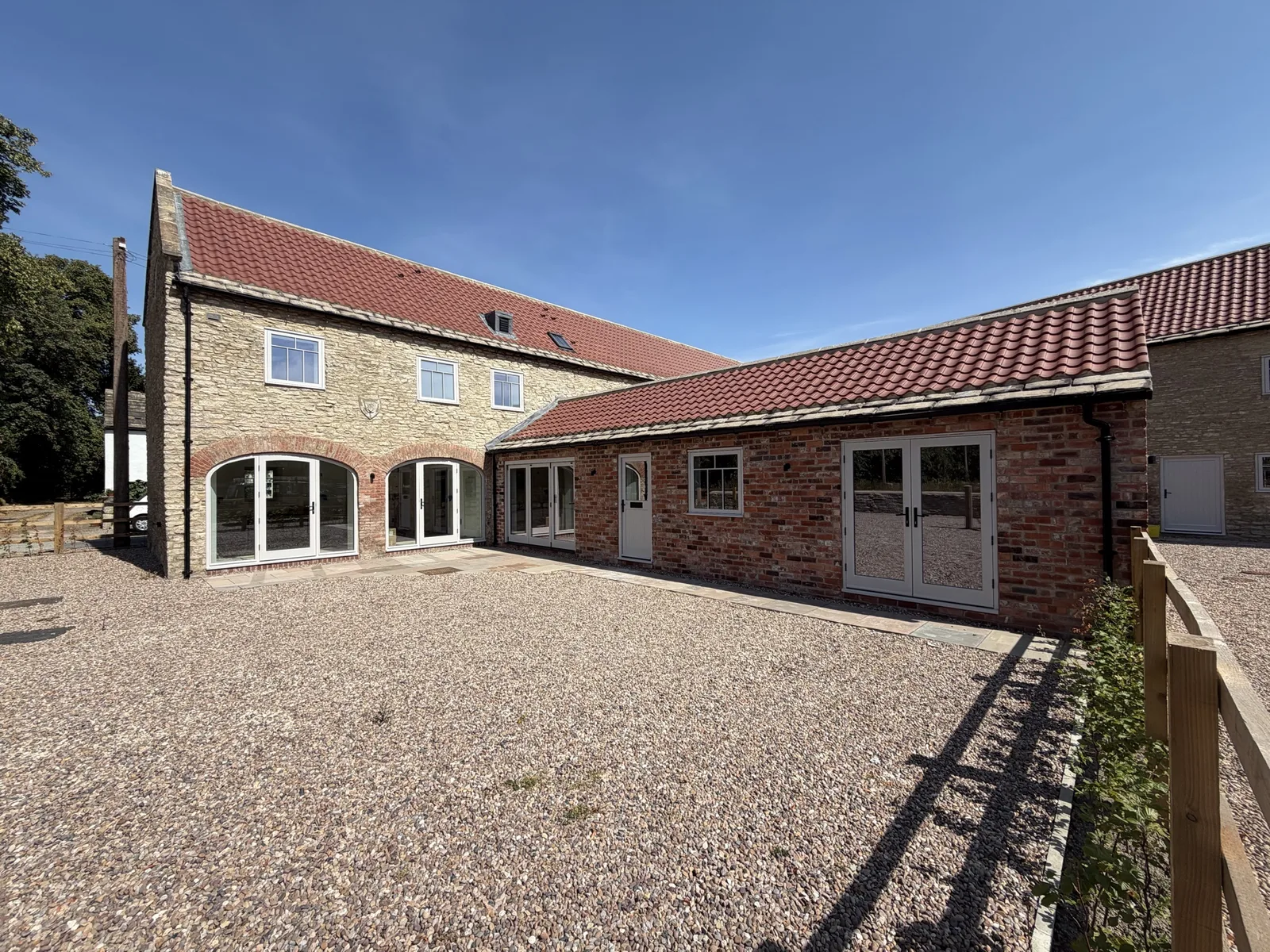Courtyard view of the barn conversion with two arched-head glazed doors in the stone wing and French doors in the brick wing