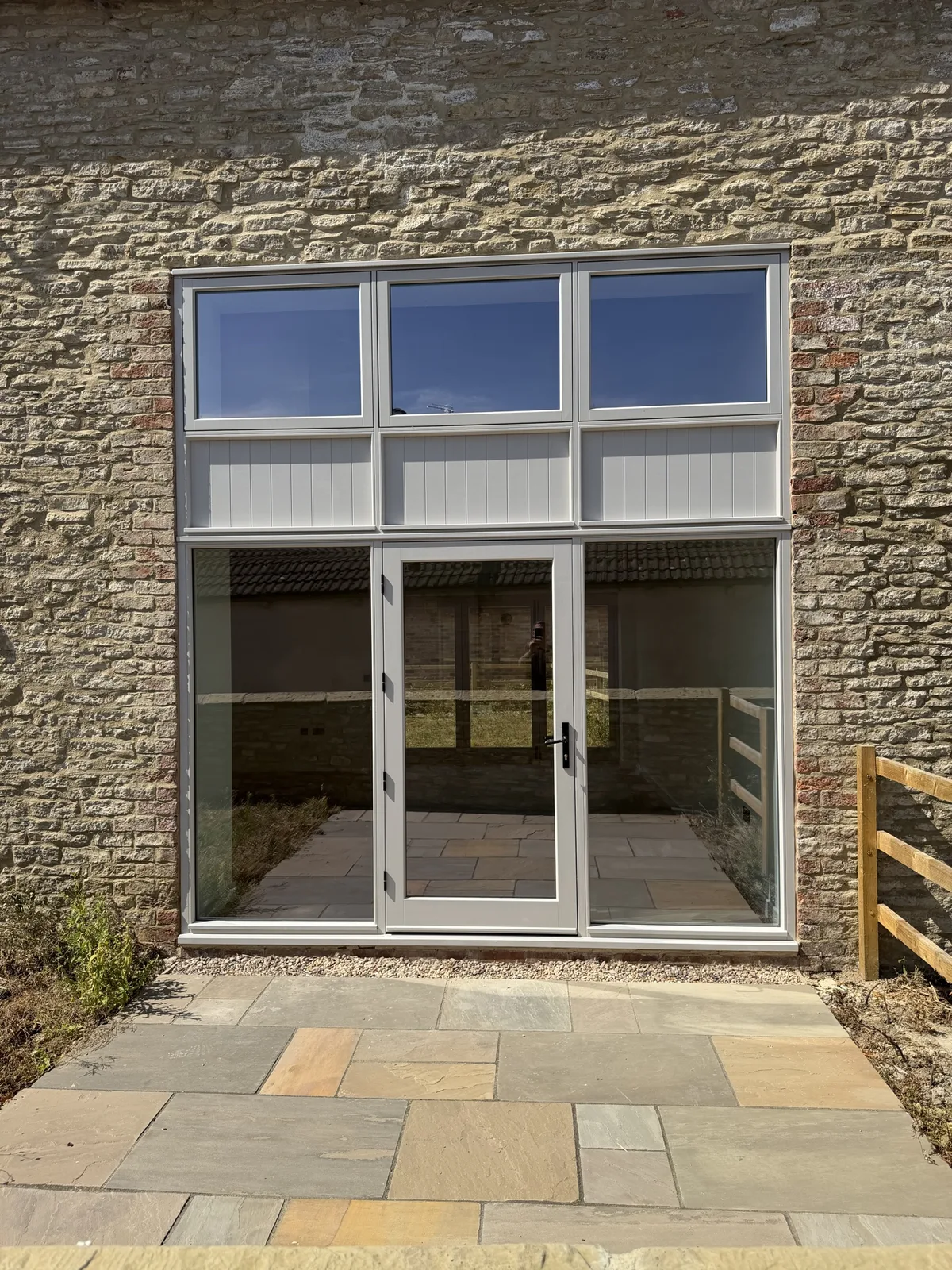 Full-height hardwood glazed screen with central glazed doors, fanlights and boarded panels in a stone barn wall